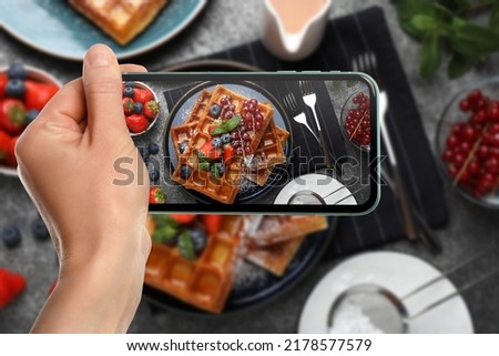 Woman taking picture of delicious Belgian waffles with berries served on grey table, top view
