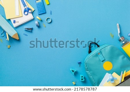 Top view photo of backpack notebooks pencil-case scissors drink bottle plastic alphabet letters binder clips plane shaped sharpener pens adhesive tape stapler ruler calculator isolated blue background