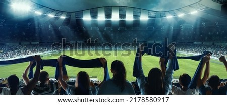 Waiting for beginning. Back view of football, soccer fans cheering their team with colorful scarfs at crowded stadium at evening time. Concept of sport, cup, world, team, event, competition Royalty-Free Stock Photo #2178580917