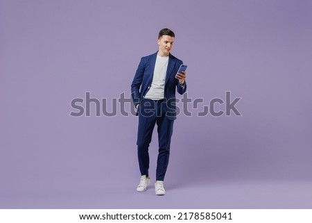 Full size young successful employee business man lawyer 20s wear formal blue suit white t-shirt move stroll hold use mobile cell phone hand in pocket isolated pastel purple background studio portrait Royalty-Free Stock Photo #2178585041