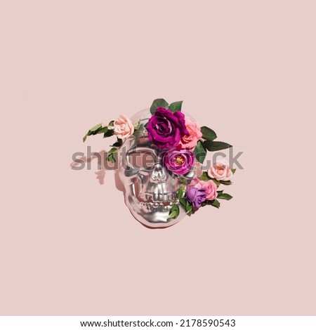 Metallic human skull mask creatively decorated with colorful flowers. Goth style layout, pastel pink background. 