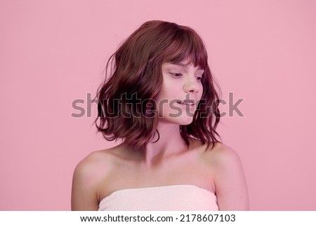 a close portrait of a sweet, happy woman standing on a pink background with pink lighting from the side, with beautiful, wave-styled hair, looking at the bottom of the frame
