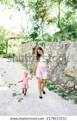 Mom with a little girl walk along the path past the stone wall in the park