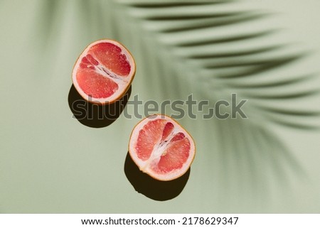 Fresh healthy grapefruit slices on green background with palm leaf shadow. Creative minimal concept, summer food, vacation, holiday. Top view, flat lay, copy space