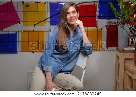 Smiling woman designer student or teacher in classroom with color palette sitting on chair and looking up