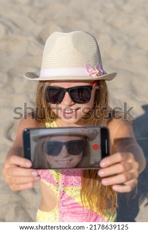 Girl makes a portrait on a smartphone on the beach. Vertical shot.