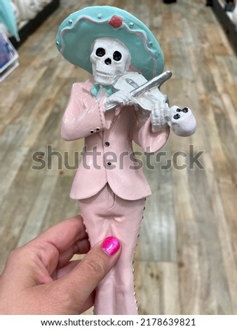 The top down, close up view of a skeleton ornament. It is wearing a pine suit, a blue hat, and is playing a violin.