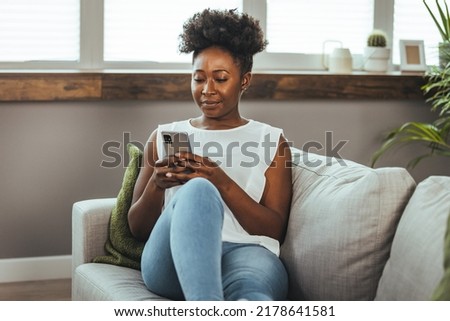 Cropped shot of an attractive young woman using her cellphone while sitting in the living room during the day. Keeping her social media fans updated