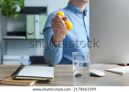 Man squeezing antistress ball while working with computer in office, closeup Royalty-Free Stock Photo #2178663399