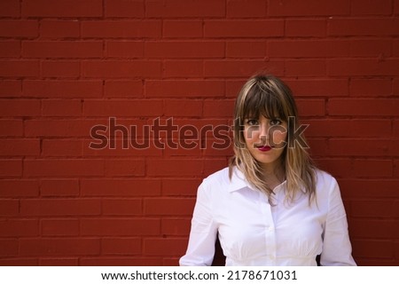Pretty, blonde, young woman having fun making different expressions in front of a red background wall. Concept various expressions. Laughter, sadness, tired, angry, hate.