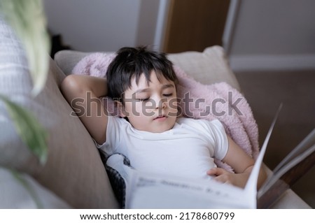 Happy School kid lying on sofa reading a book with morning light shining from window. Child boy reading story relaxing at home on weekend, Positive children concept