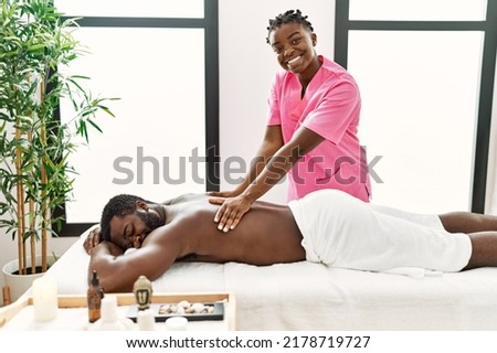 Young physiotherapist woman smiling happy giving back massage to african american man at the clinic. Royalty-Free Stock Photo #2178719727