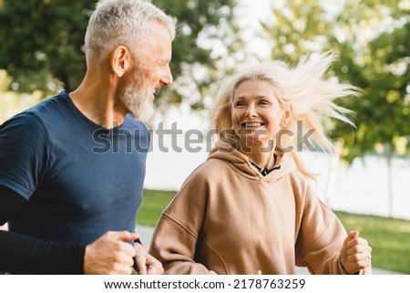 Mature middle aged senior couple running together in the park stadium looking at each other while jogging slimming exercises. Training workout Royalty-Free Stock Photo #2178763259