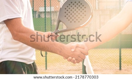 Male padel players handshake after win a padel match in a green paddel court outdoor. Tennis players shake hands with shining sun bright flash