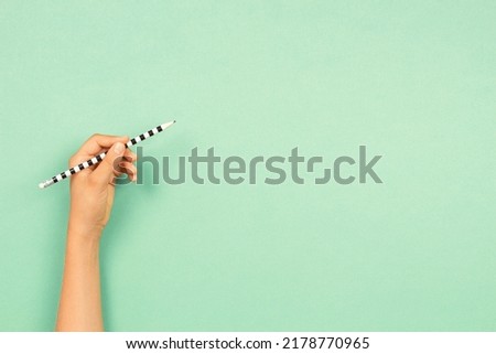 Left hand holding pencil for writing over light green background. Left Handers Day Royalty-Free Stock Photo #2178770965