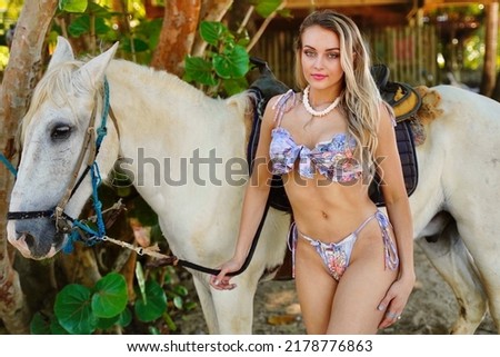 Female model in bikini by white horse
