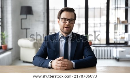 Head shot confident businessman wearing suit and glasses speaking looking at camera, sitting at work desk in office, mentor coach shooting webinar, hr manager holding online interview with candidate Royalty-Free Stock Photo #2178786093
