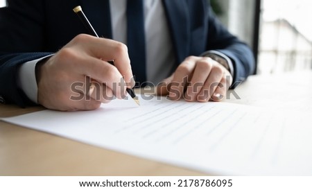 Close up business owner business man wearing suit signing documents, filling form, making successful deal, sitting at office desk, employee candidate signing job agreement after interview
