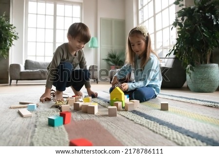 Close up little girl and boy playing with colorful wooden blocks and toy dinosaurs, sitting on warm floor with underfloor heating, curious cute sibling having fun at home together, enjoying weekend Royalty-Free Stock Photo #2178786111