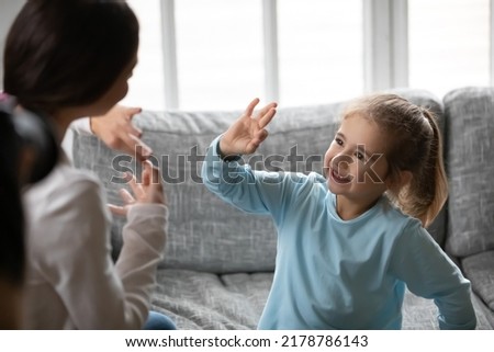 Close up smiling deaf little girl communicating with mother, speaking sign language, sitting on couch at home, therapist teaching little girl, talking nonverbal, hearing disability concept Royalty-Free Stock Photo #2178786143