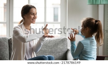 Close up smiling mother and adorable deaf daughter communicating, speaking sign language, sitting on couch at home, therapist teaching little girl, talking nonverbal, hearing disability concept Royalty-Free Stock Photo #2178786149