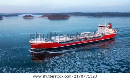 LNG powered oil and chemical tanker making way ahead in Finnish archipelago during winter morning sunrise. Haze in the air and sea surface covered in light ice floes. Aerial side view Royalty-Free Stock Photo #2178791323
