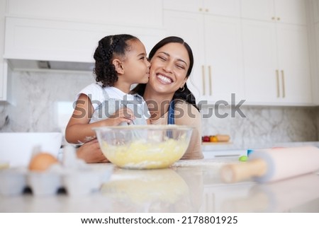 Mother and daughter baking together in a home kitchen. Caring small adorable little girl kissing her single mother on the cheek. Happy woman and affectionate child bonding inside and learning to cook
