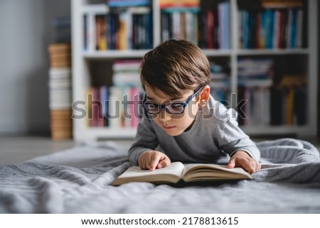 One caucasian boy lying on the floor at home in day reading a book front view wearing eyeglasses copy space real people Royalty-Free Stock Photo #2178813615