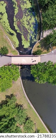 An aerial drone shot, taken over a quiet park. In view are the reflective waters of the pond and the walkways around it. It was shot on a sunny morning in Valley Stream, NY in the summer.