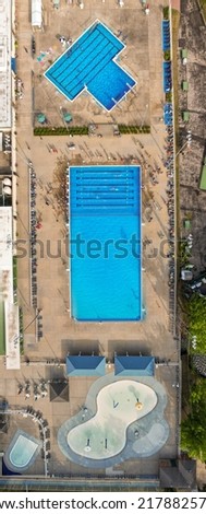 A top down shot, taken directly over two pools. There are people in view and it looks like one pool is opened for a competition. The picture was taken, using a drone camera.
