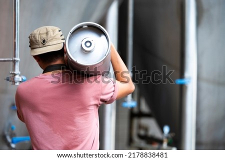 Young man in leather apron holding beer keg at modern brewery, craft brewery worker Royalty-Free Stock Photo #2178838481