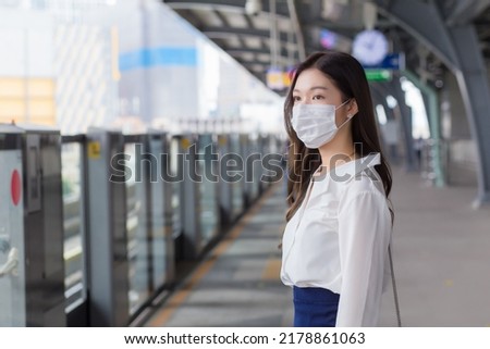 Asian professional business female with long hair wears a mask is waiting to go to workplace or office by sky train in the New Normal lifestyle. Royalty-Free Stock Photo #2178861063