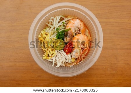 A picture bowl of Laksa Sarawak on the table. In consist of vermicelli, prawns, coconut soup gravy, chicken and eggs.