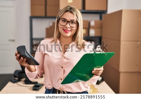 Young hispanic woman ecommerce business worker holding calculator and clipboard at office