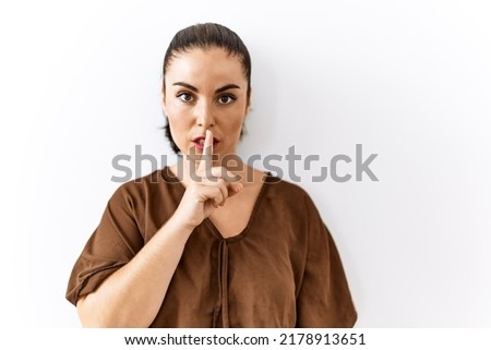 Young brunette woman standing over isolated background asking to be quiet with finger on lips. silence and secret concept. 