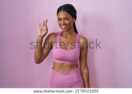 African american woman with braids wearing sportswear over pink background smiling positive doing ok sign with hand and fingers. successful expression. 