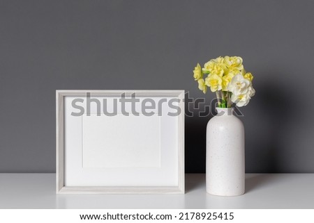 Landscape photo frame mockup with daffodils flowers in vase over grey wall
