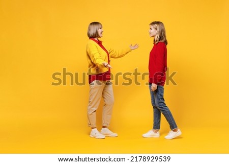 Full body cool woman 50s in red shirt have fun with teenager girl 12-13 years old. Grandmother granddaughter meeting together spread hands isolated on plain yellow background. Family lifestyle concept
