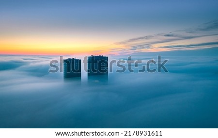 Skyscraper rooftop over the clouds at sunrise. Thick fog covers the Riga city, and warm sunlight over the clouds and church tower. Royalty-Free Stock Photo #2178931611