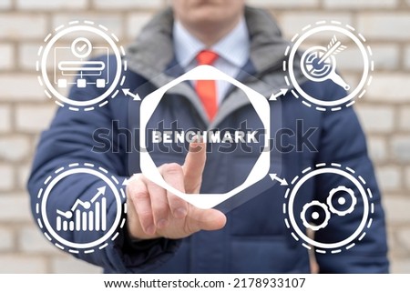 Business, technology, internet and network concept. Young businessman working on virtual touchscreen of future and presses inscription: BENCHMARK. Benchmarking.