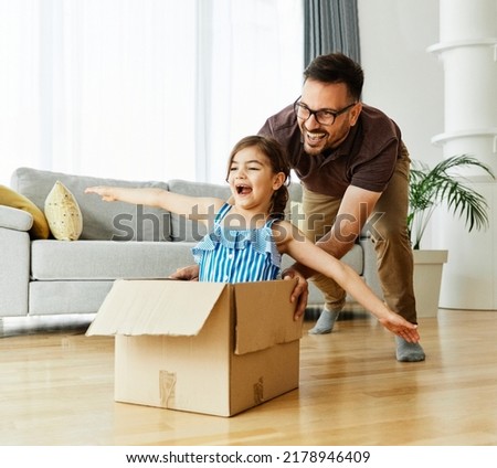 Father pushing his daughter sitting in a cardboard box, having fun at home Royalty-Free Stock Photo #2178946409