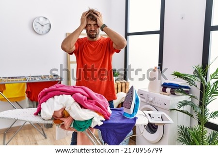 Young hispanic man ironing clothes at laundry room suffering from headache desperate and stressed because pain and migraine. hands on head. 