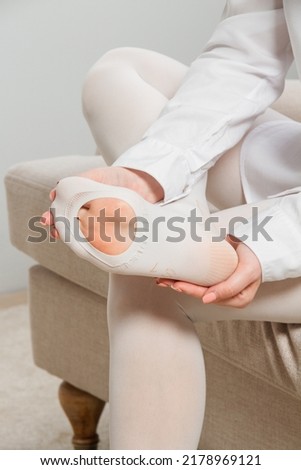 White hosiery. Beautiful long female legs in stockings. Girl putting on stockings at home in a white room. Varicose veins prevention. Woman body in underwear.