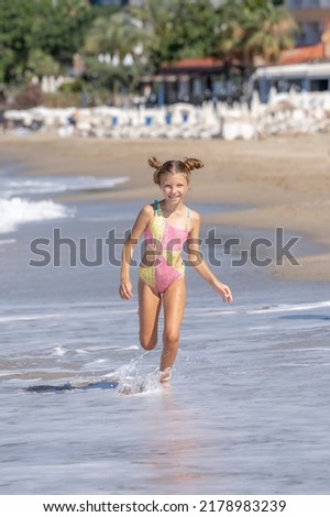 A happy little girl runs along Cleopatra Beach in Alanya, Turkey. Vertical shot.