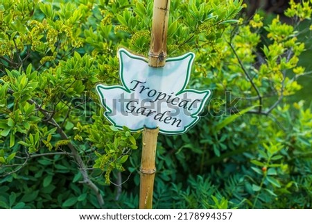 One green and white outdoor flower sign that says Tropical Garden