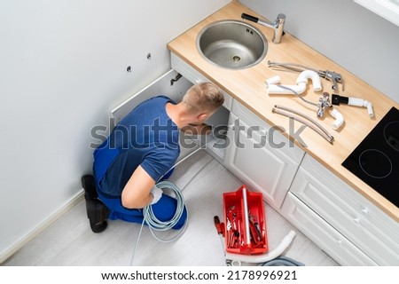 Male Plumber Cleaning Clogged Sink Pipe In Kitchen Royalty-Free Stock Photo #2178996921