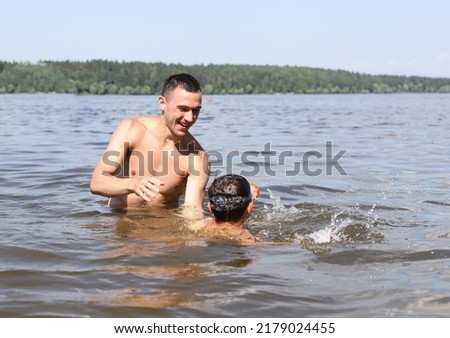 father and son swim together in a river pond