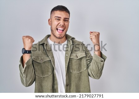 Young hispanic man standing over isolated background celebrating surprised and amazed for success with arms raised and eyes closed. winner concept. 