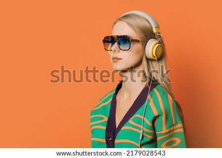 Stylish 80s woman in eyeglasses, headphones and blouse on orange background