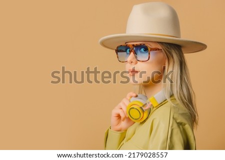 Stylish 80s woman in eyeglasses, headphones and hat on brown background